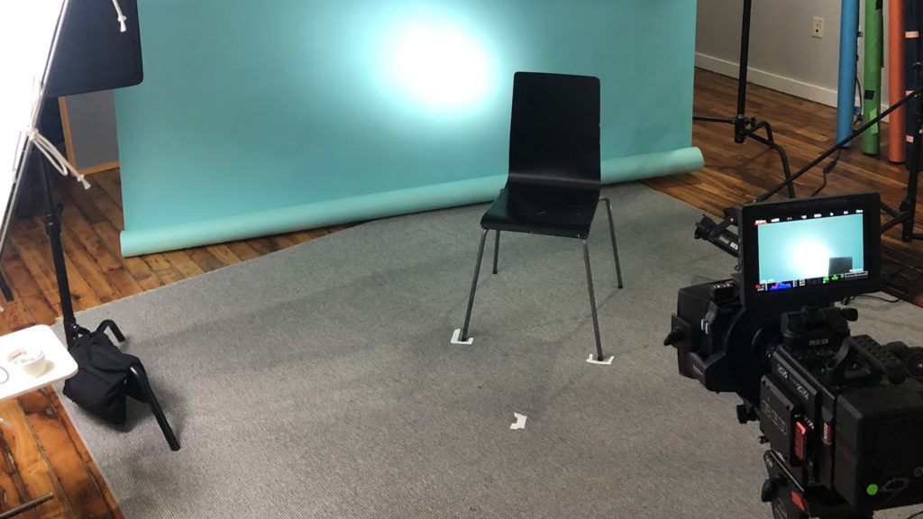 behind the scenes of the documentary interview set up featuring the camera and lighting and an empty chair waiting for the person to be interviewed 